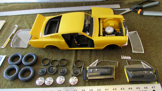 A model kit of a yellow classic sports car with all of the pieces laid out neatly on a table